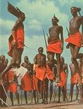 photo of a group of tall, slender, young East African men in traditional tribal clothing dancing together with their spears--they are jumping vertically more than 3 feet