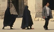 photo of two Moslem women covered from the top of their heads to their feet with black loose gowns that cover up their body; a Moslem man in European style clothes is walking in front of them