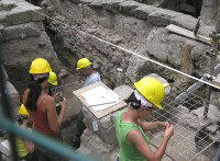 photo of archaeologists working in a trench next to a wall mapping and excavating an ancient building