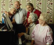 photo of five elderly North Americans singing together at a piano