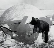 Early 20th century photo of an Eskimo man building an igloo (winter ice house)
