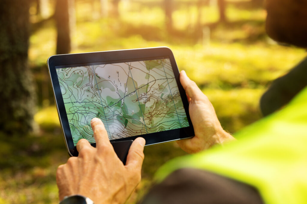 A surveyor using a digital tablet to view a topographic map while working in a forest.