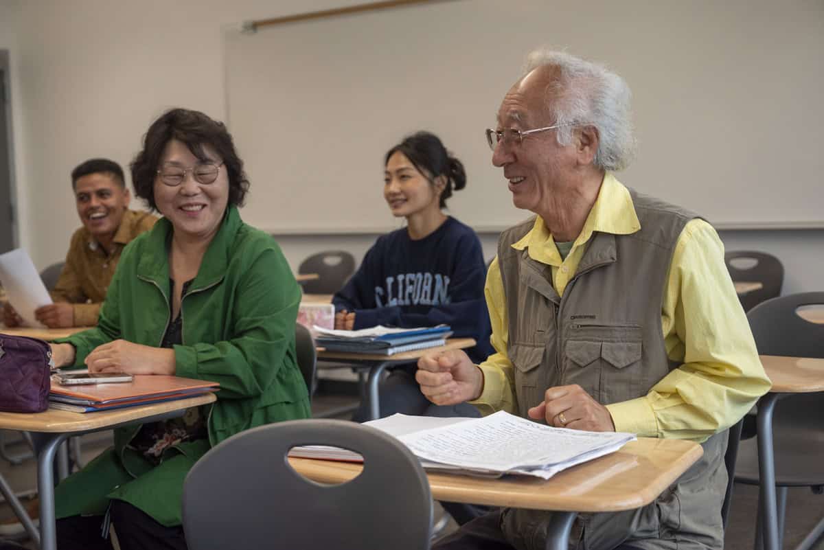 Adult students participate in an English language learning class, engaging in discussion and coursework together.