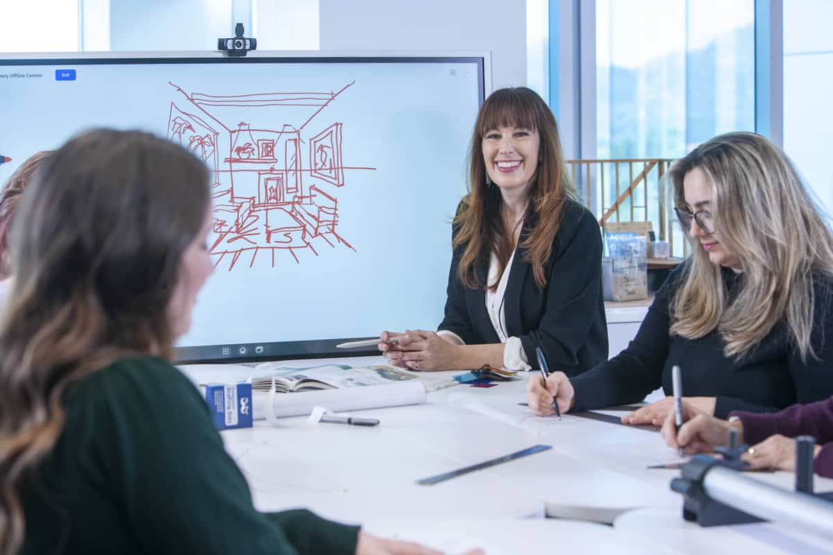 Interior design instructor leads a classroom discussion using a digital display while students take notes.