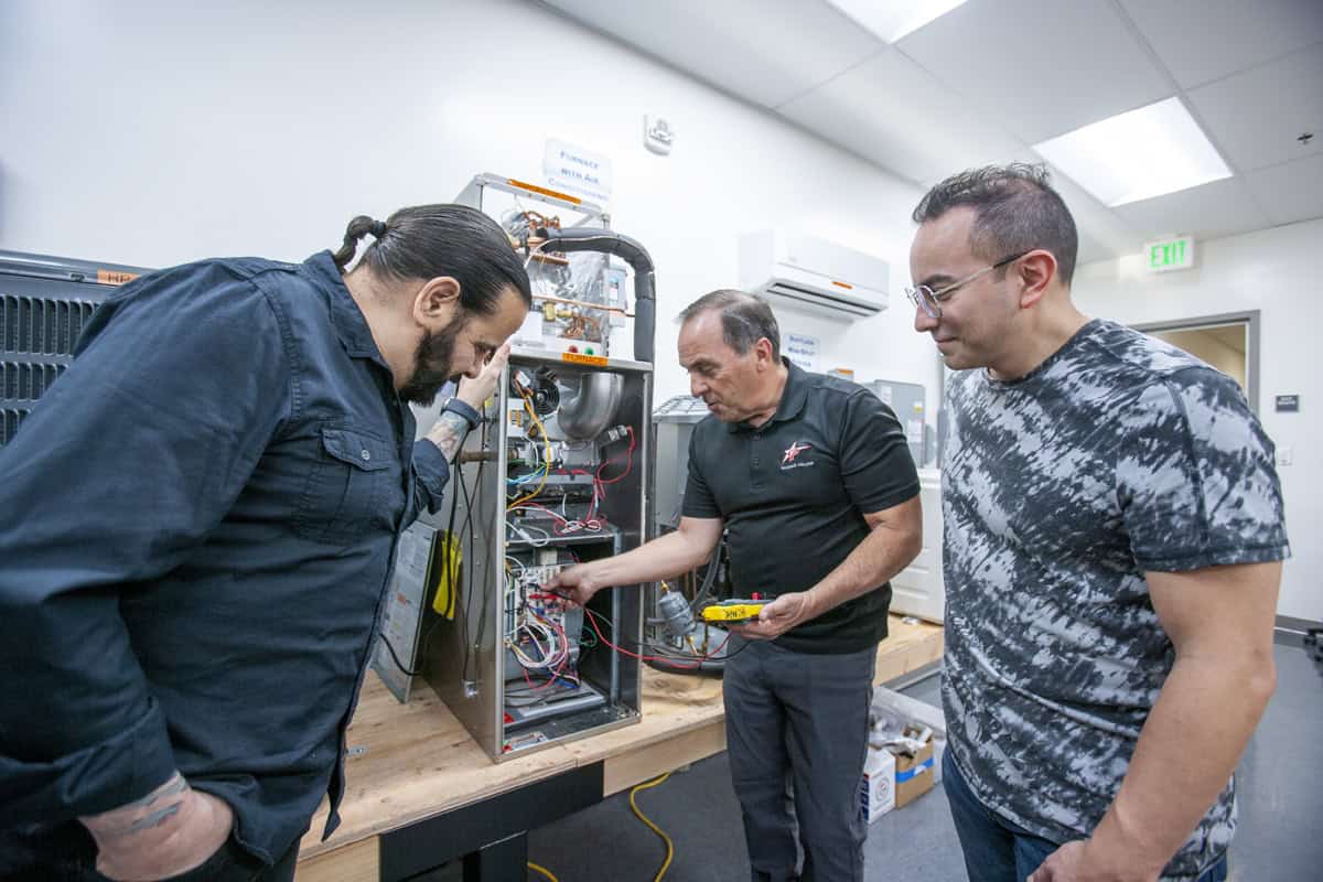 HVAC instructor demonstrates electrical diagnostics on heating and cooling equipment while students observe.