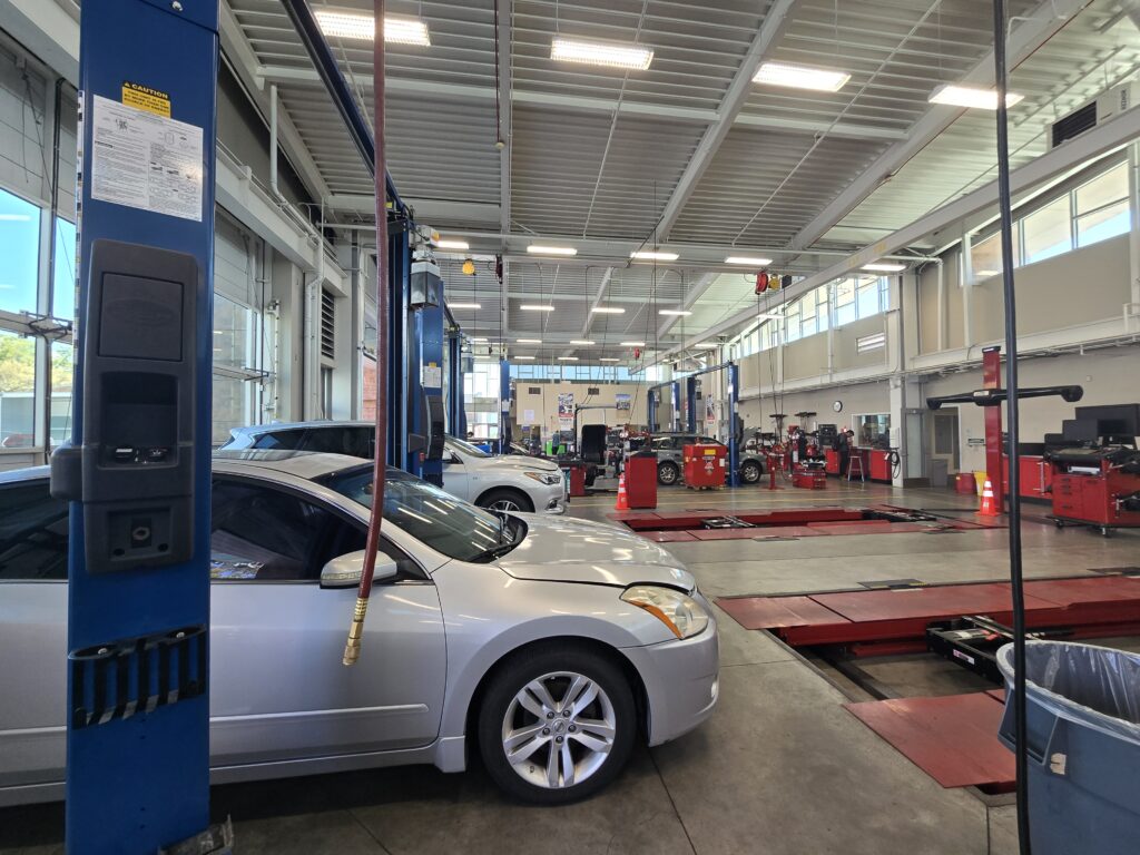 A modern, clean automotive repair bay at the Palomar College Automotive Technology facility, featuring a silver sedan parked next to professional blue car lifts and red alignment racks.