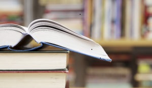 Open textbook on a stack of books in front of library shelves