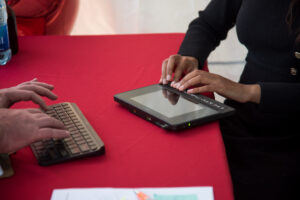 Close up of Haben Girma’s hands on her keyboard assistive technology against a red tablecloth.