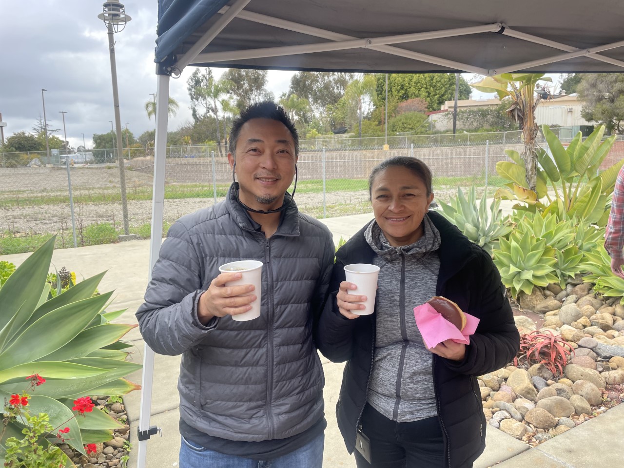 A man and a woman smile holding coffee and donuts.