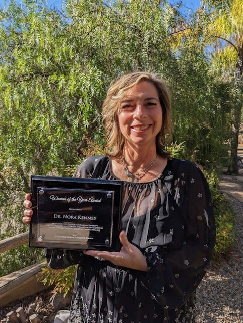 Dr. Nora Kenny photo with award in front of a tree. 