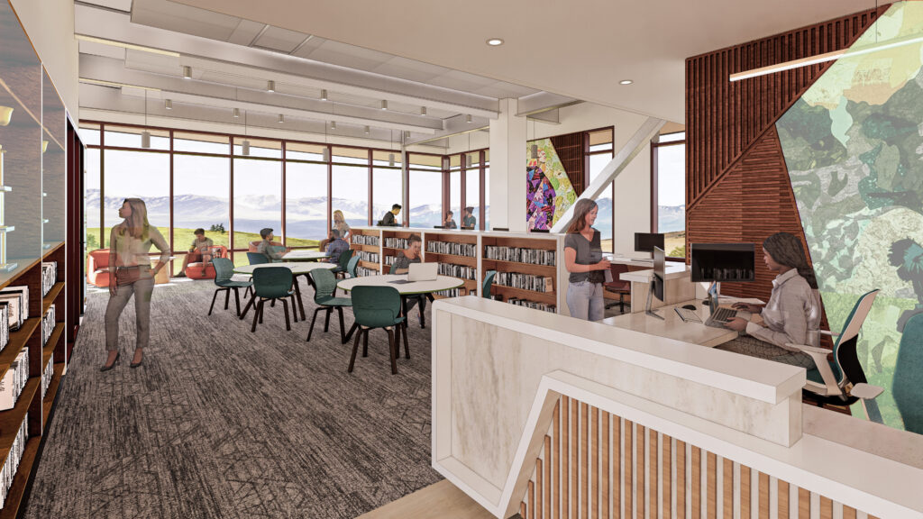 Library interior with service desk, bookshelves, study tables, large windows, and views of the surrounding landscape.