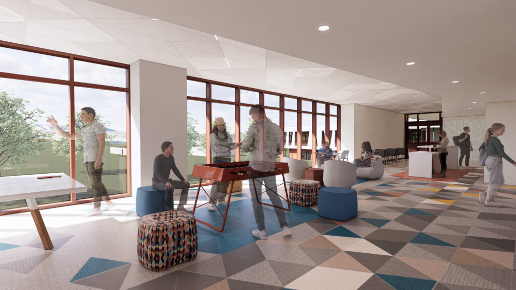 Student lounge with open seating areas, patterned flooring, and large windows providing outdoor views.