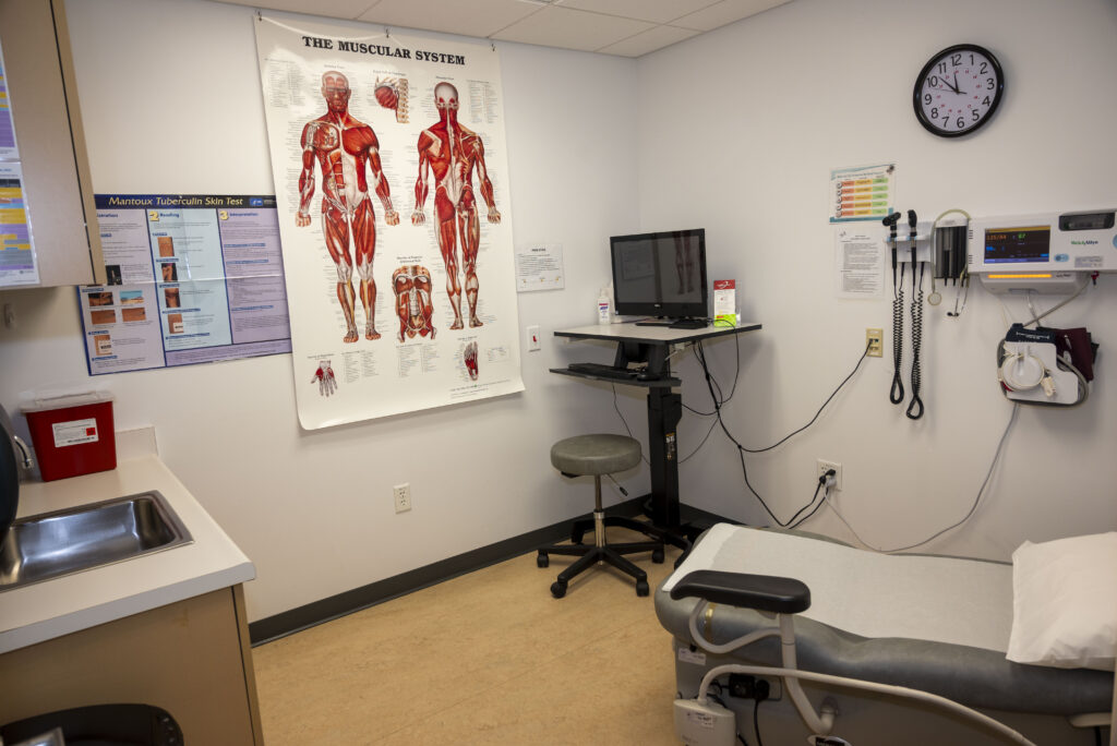 Exam table, computer, sink with wall poster of the Muscular System inside Student Health Center exam room