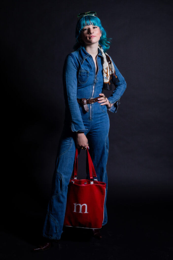 Female fashion model in denim top and pants with red cloth shopping bag in right hand.
