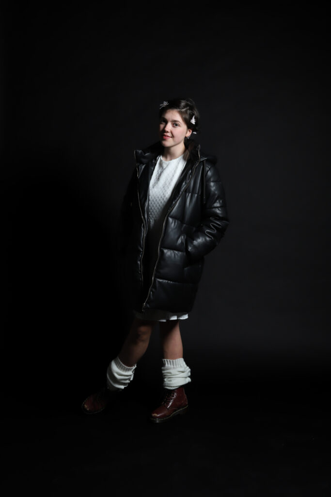 Female fashion model in black coat with white leg warmers and brown boots.