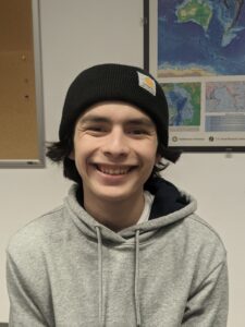 Josh Miranda wears a light gray hoodie and a black beanie inside a classroom.