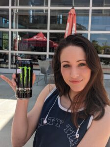 Katherine Regalado holds a Monster energy drink and wears a dark blue top and Apple earpods.