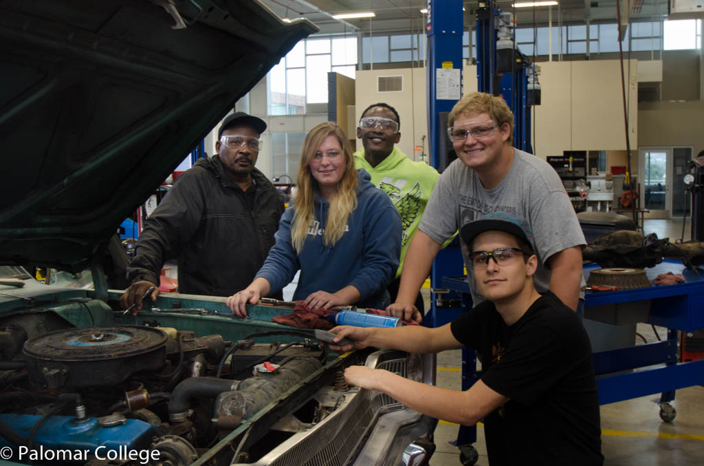 Five students in the Auto Technology Lab, wearing safety glasses and inspecting a car engine