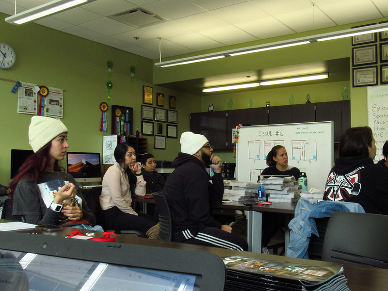 Students set at a conference table in the newsroom at Palomar College. They are sitting next to a white board that reads, Issue #6.