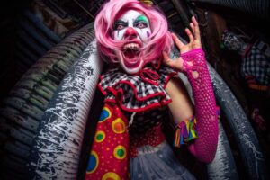 A scary clown with pink hair and sharp teeth poses for the camera