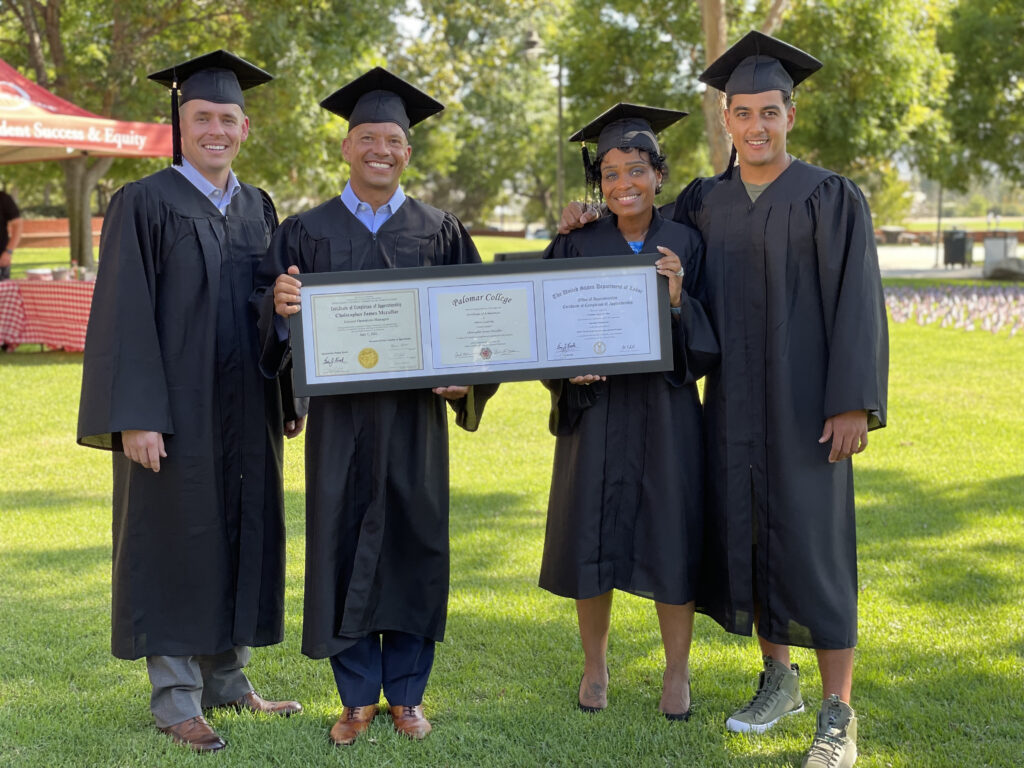 Photo of the first four graduates from the Palomar College Military Leadership program, wearing their graduation robes and holding their three, framed certificates. 