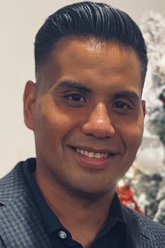 Headshot of John Mendoza with a Christmas tree.