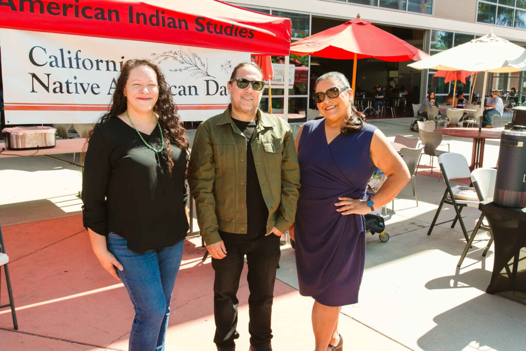 Three individuals standing in front of a red canopy with a banner reading 'California Native American Day.'