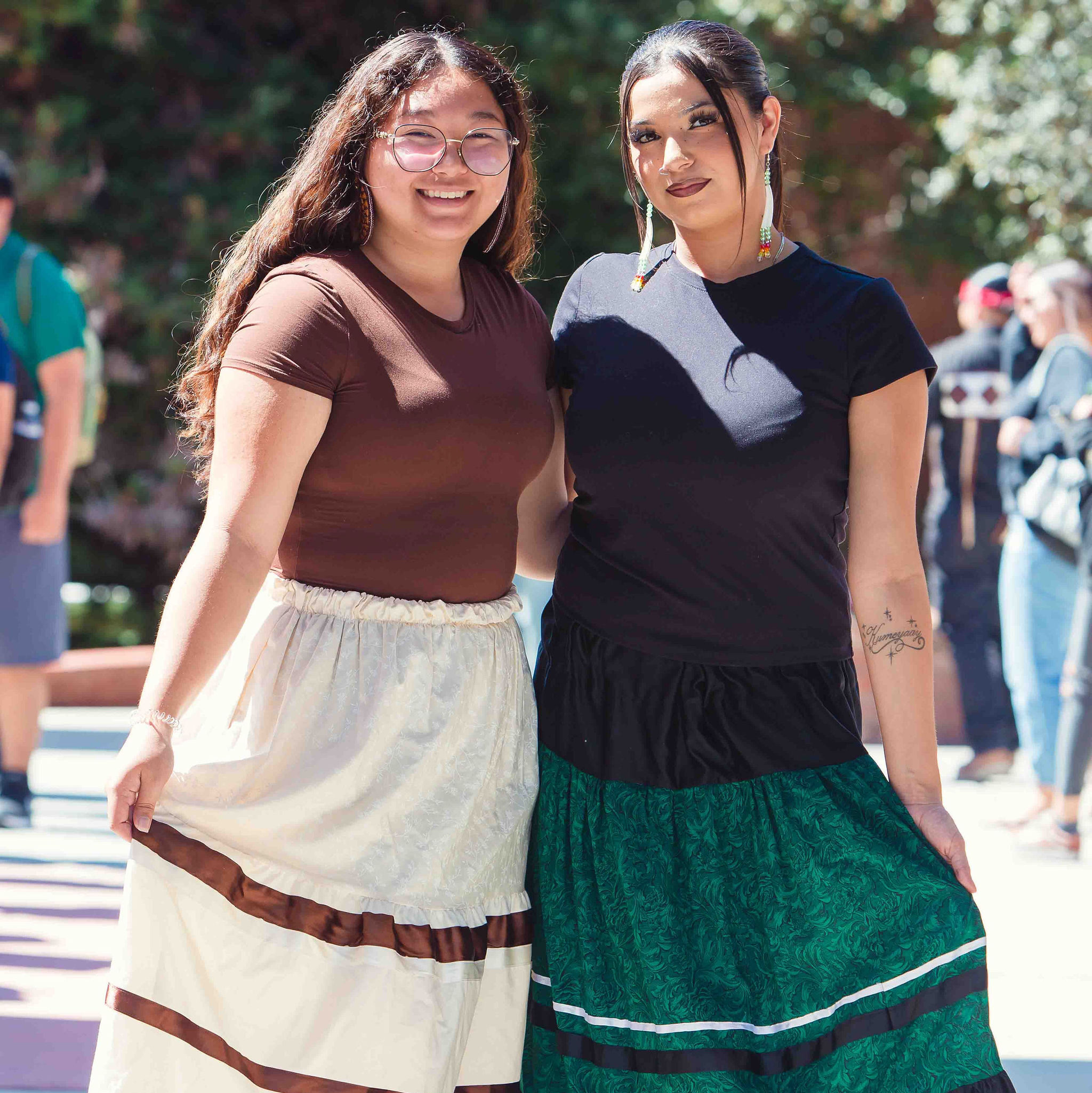 Two individuals wearing ribbon skirts standing outdoors during California Native American Day.