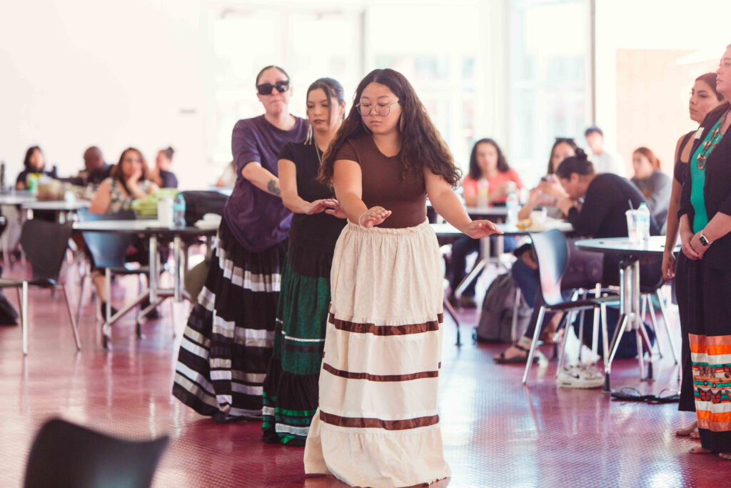 Bird dancers guiding attendees through traditional dance steps indoors during California Native American Day.