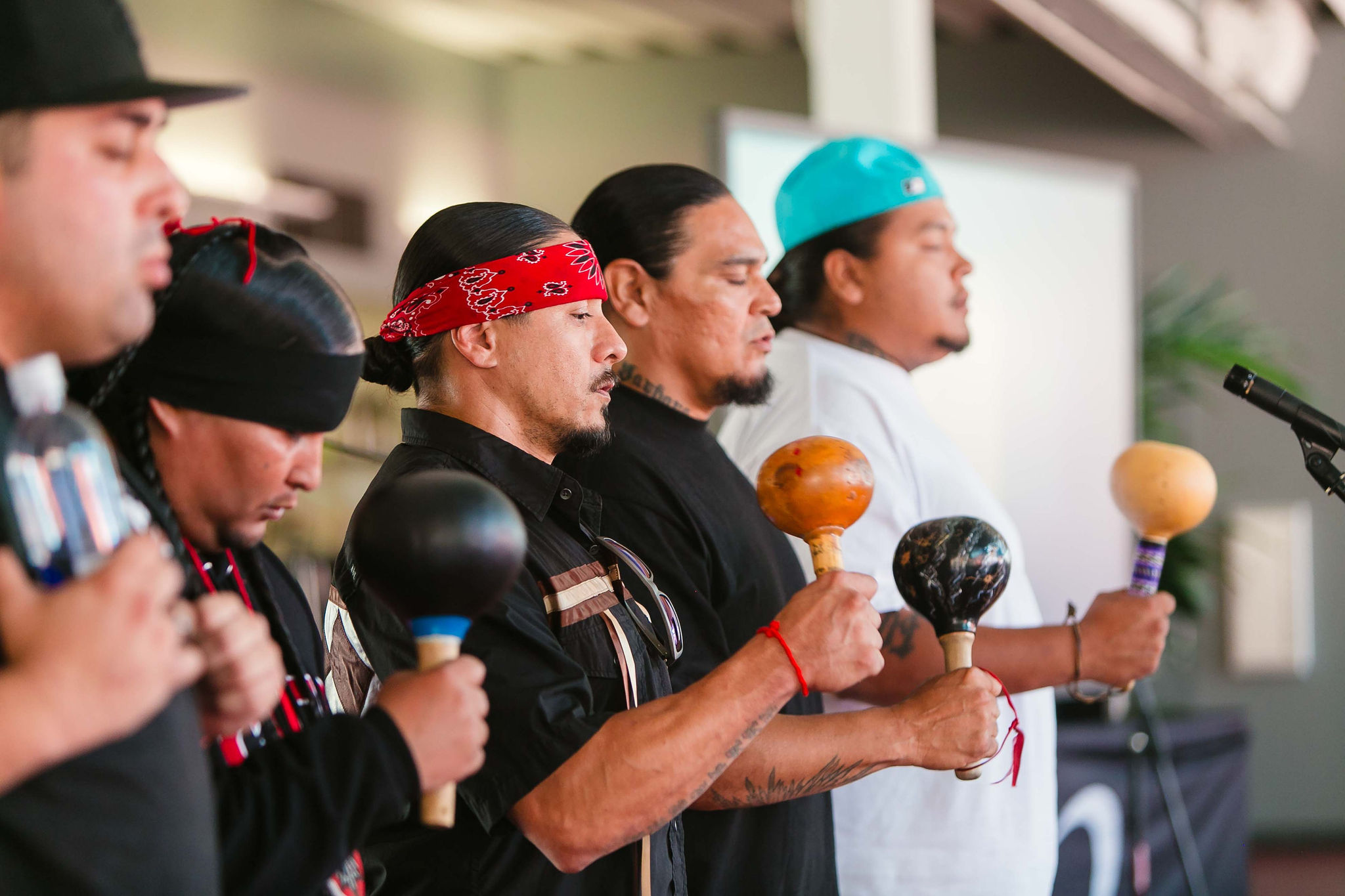 Opening Blessing by Bird Singers Bird singers holding rattles and singing near a microphone indoors to begin California Native American Day.