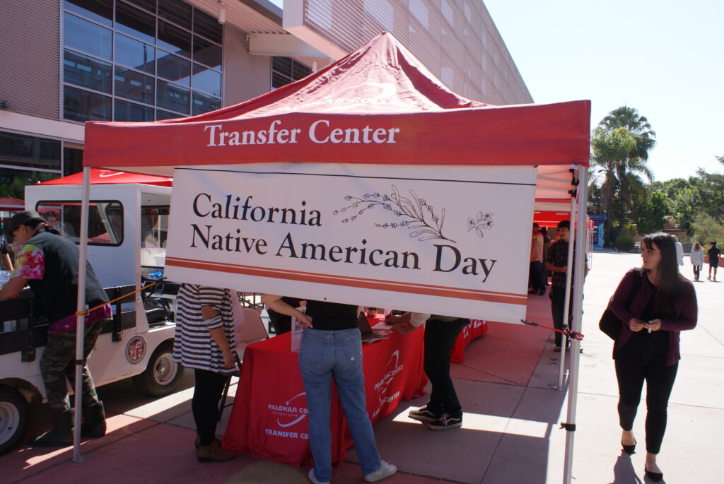 A large banner reading "California Native American Day" displayed on a red Transfer Center canopy outdoors.