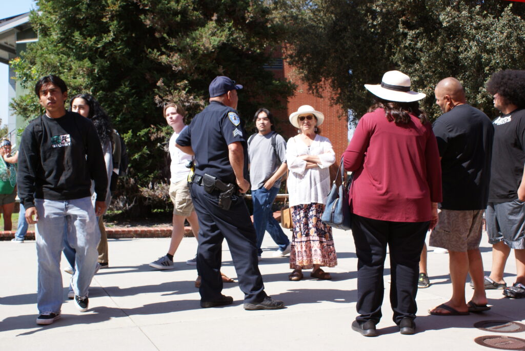 A campus safety officer speaking with attendees outdoors near trees and event booths.