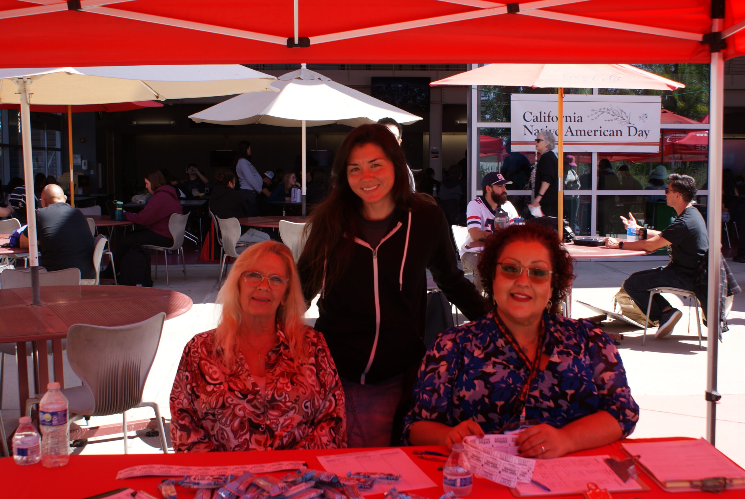 Community Engagement Table A table with two people seated and informational materials under a red canopy at the event.