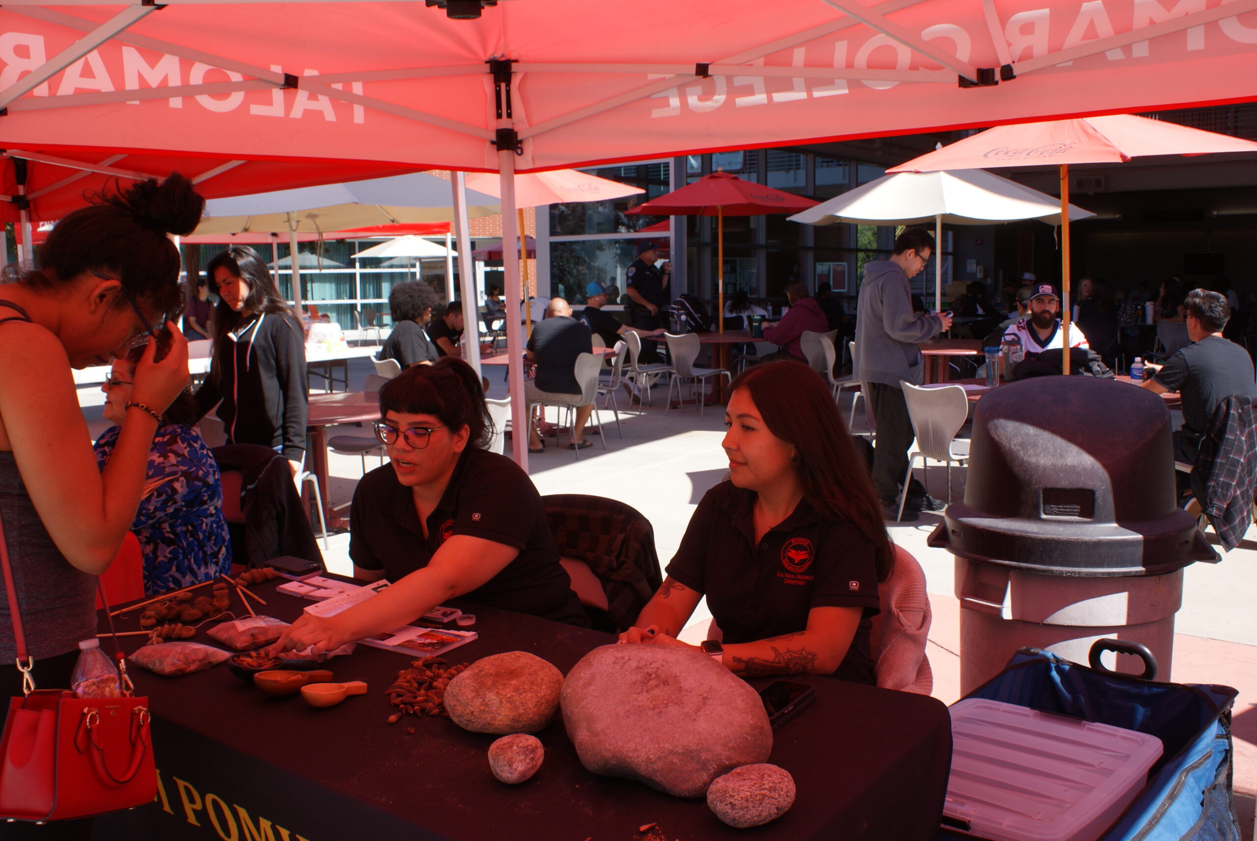 Cultural Demonstration at Na$Xayam Pomki Museum Table A participant interacts with museum representatives at a table featuring grinding stones and seeds under a red canopy.