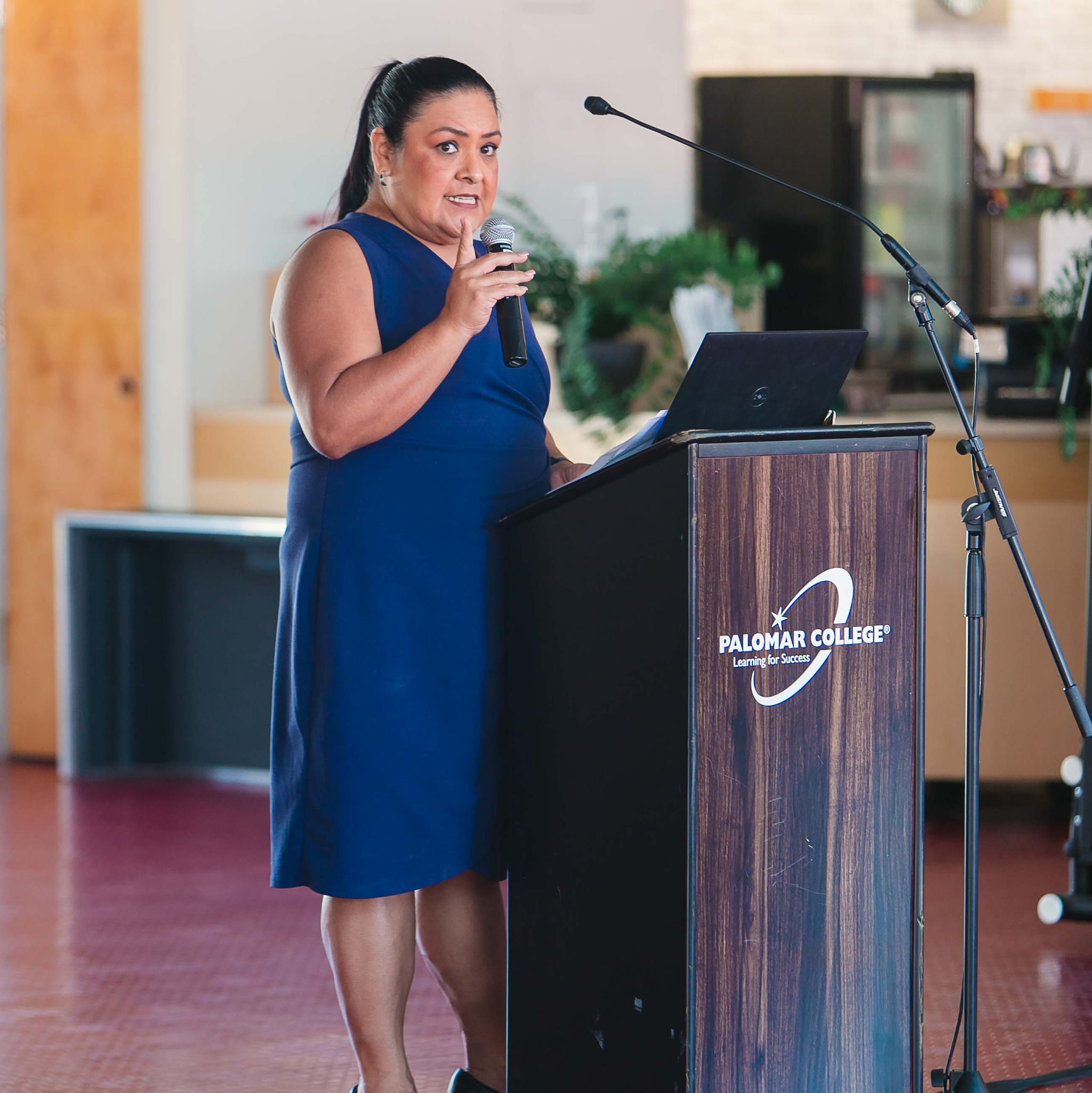 Individual speaking at a podium with a microphone indoors during cultural event.