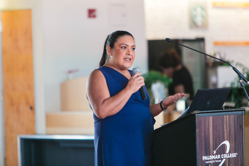 Individual holding a microphone and speaking indoors during California Native American Day.