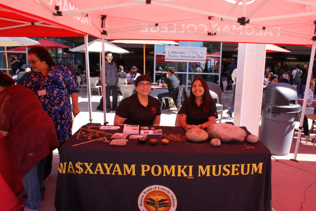 A table with traditional grinding stones and seeds under a canopy labeled Na$xayam Pomki Museum.