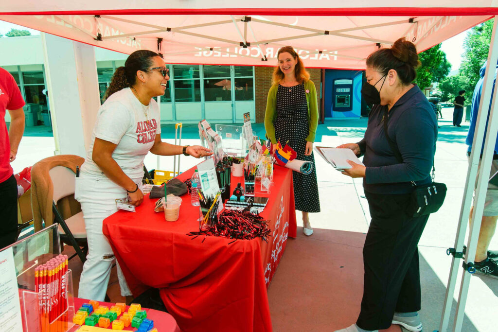 Individual standing at a table with informational materials under a red canopy.