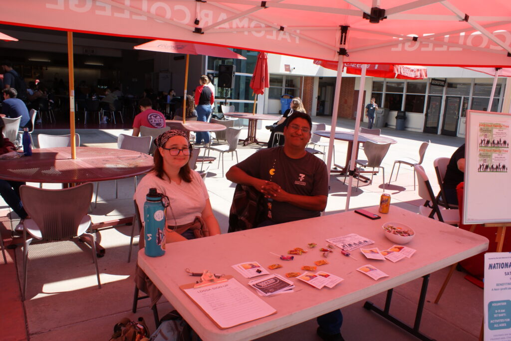 A table with informational flyers and small items under a red canopy at California Native American Day.