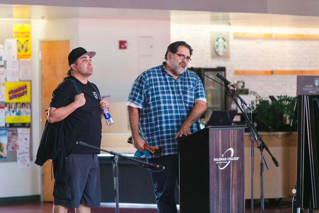 Two individuals speaking indoors near a podium during California Native American Day.