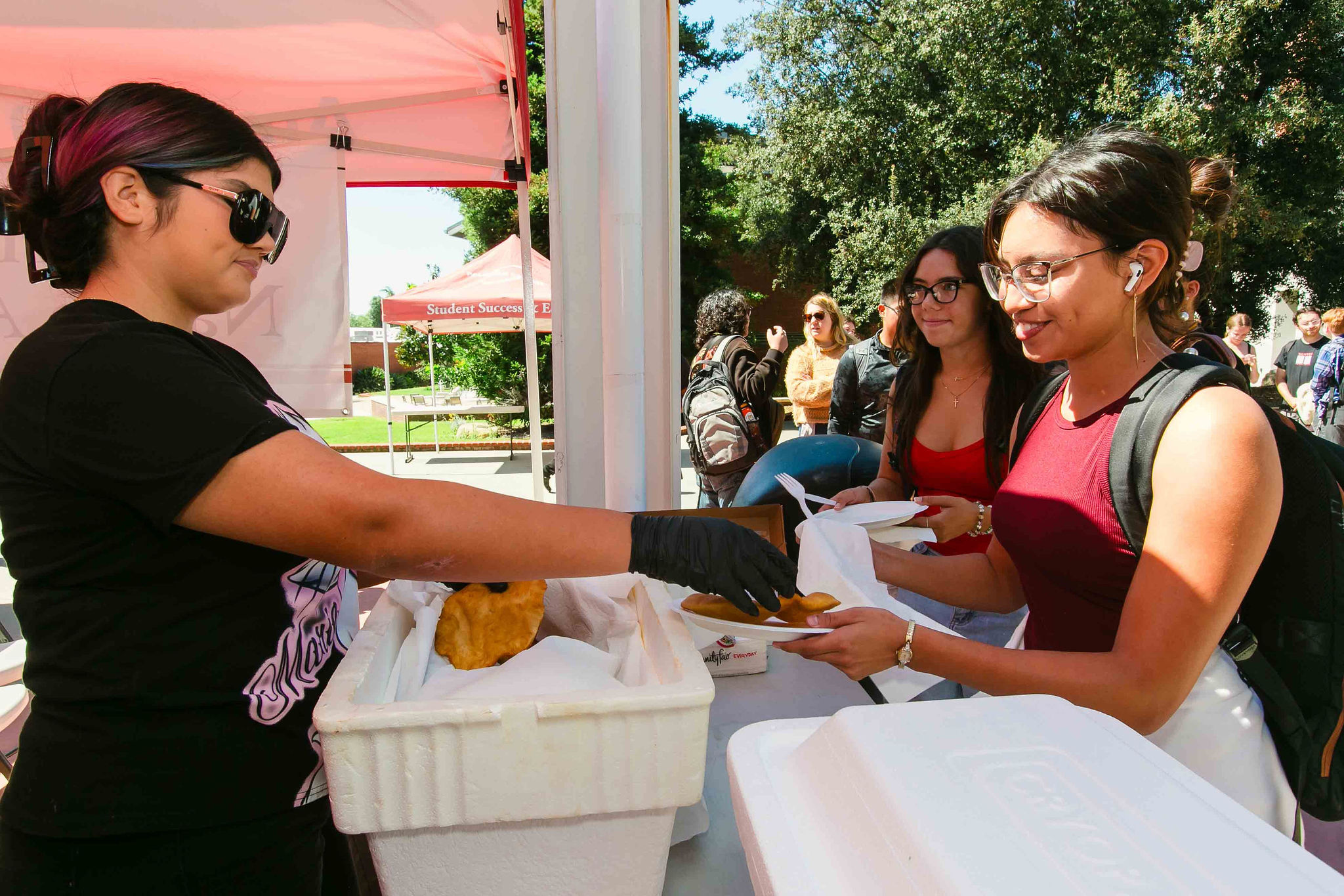 Serving Frybread to Attendees Individual wearing gloves handing a plate of frybread to another person at an outdoor food station.