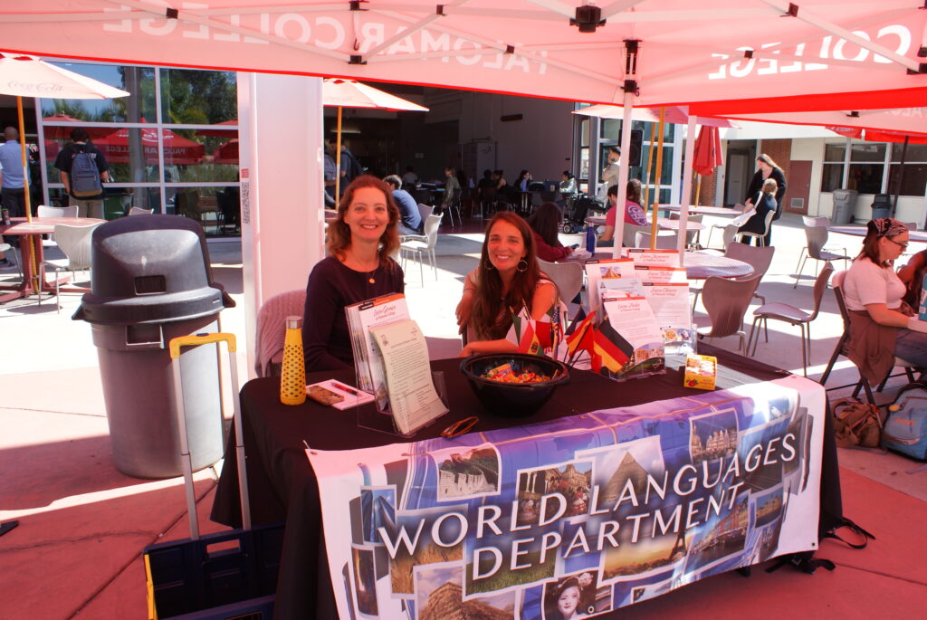 A table with a colorful banner for the World Languages Department featuring brochures and small flags under a red canopy.