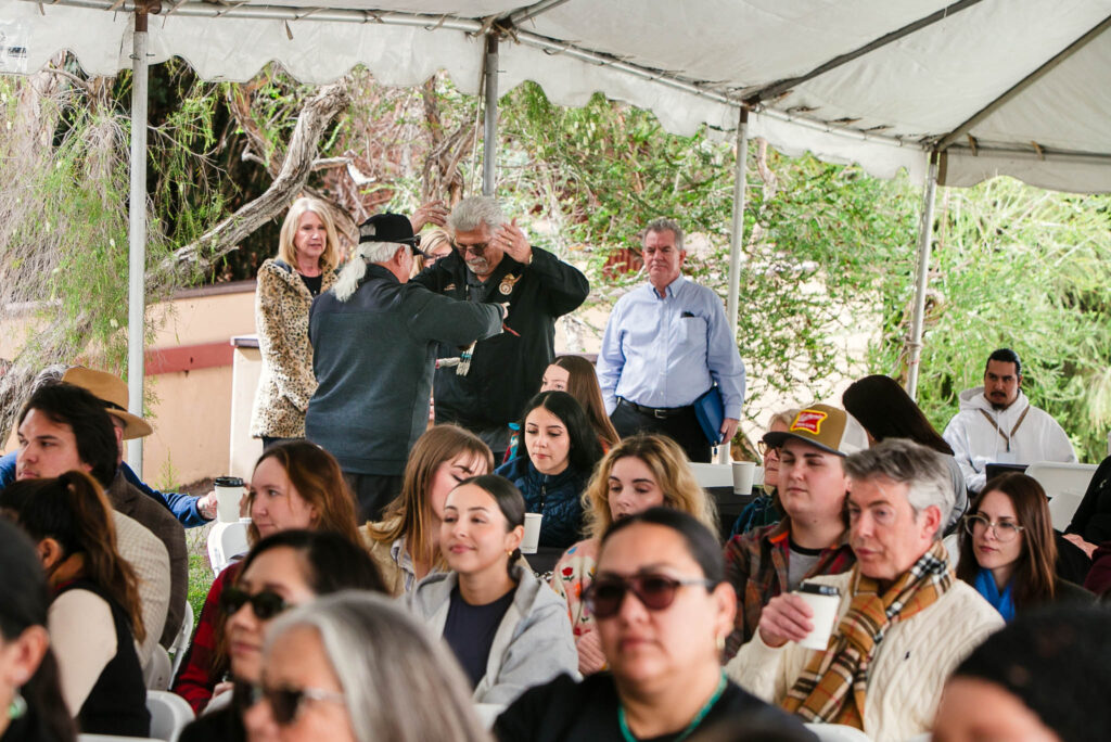 A person holding a feather walking between rows of seated attendees under a large white tent.