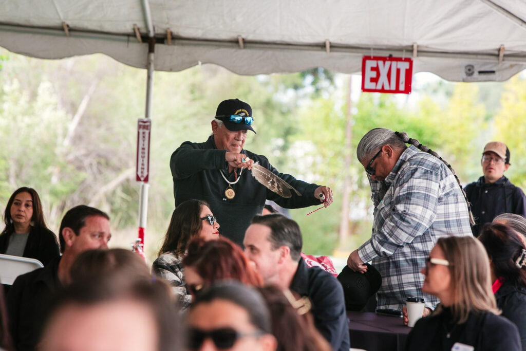 A person holding a feather moving past seated attendees inside a tented event space.