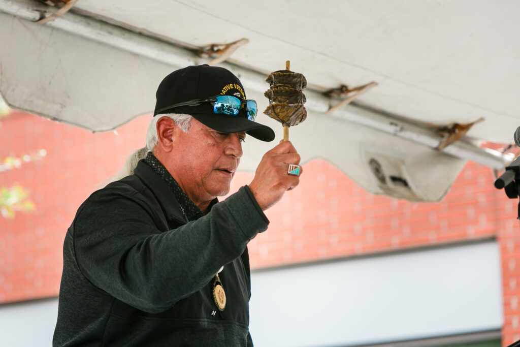 A person on stage under a tent holding an object and addressing the audience.