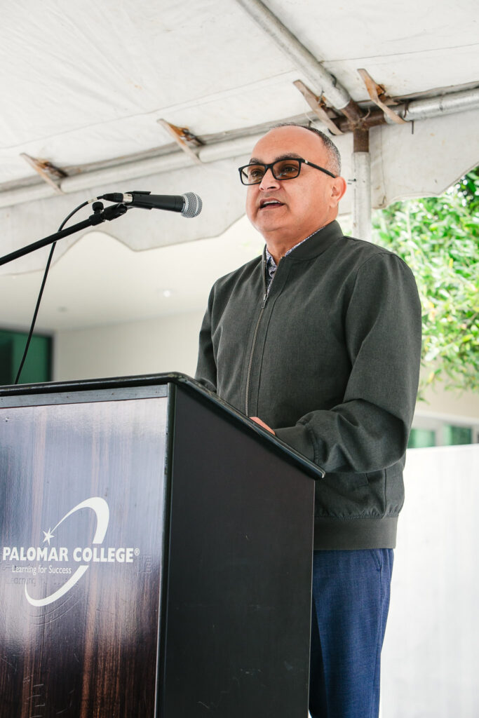 A person at a podium speaking into a microphone under a large outdoor tent.