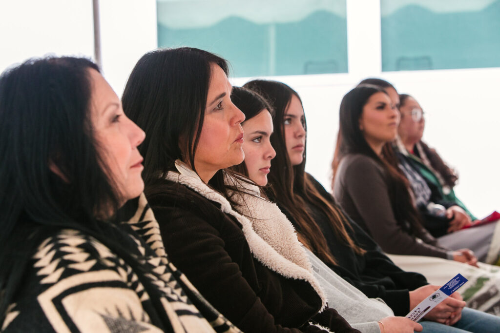 A row of attendees seated under a tent holding tickets and looking toward the stage.