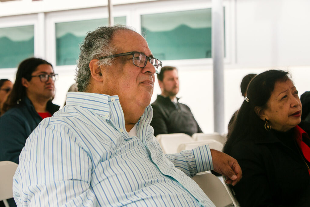 Two people seated among the audience under a large white tent during the ceremony.