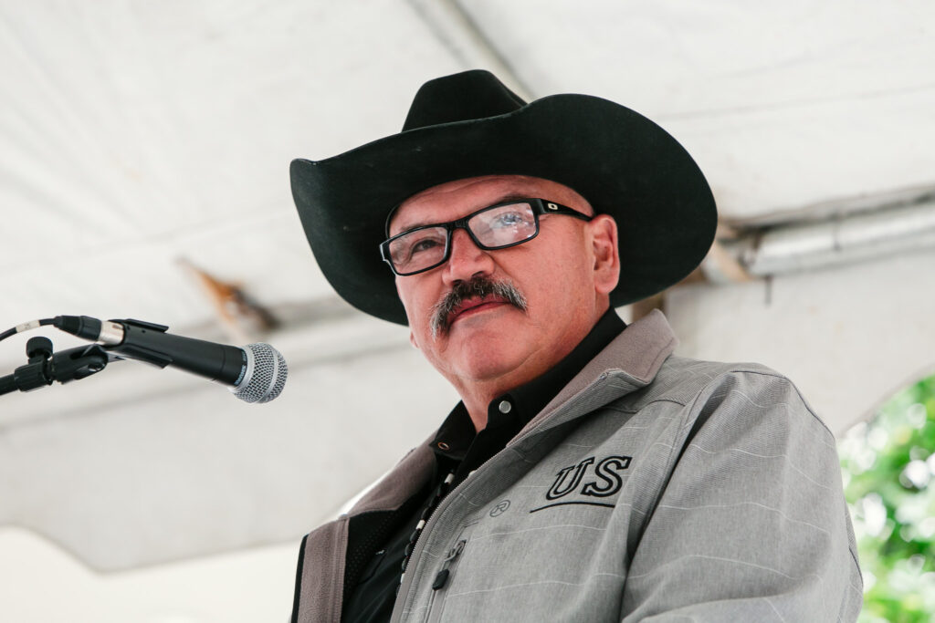 A person wearing a cowboy hat standing near a microphone under an outdoor event tent.