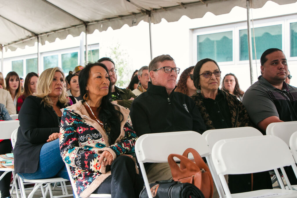 Attendees seated under outdoor event tent listening to speaker.